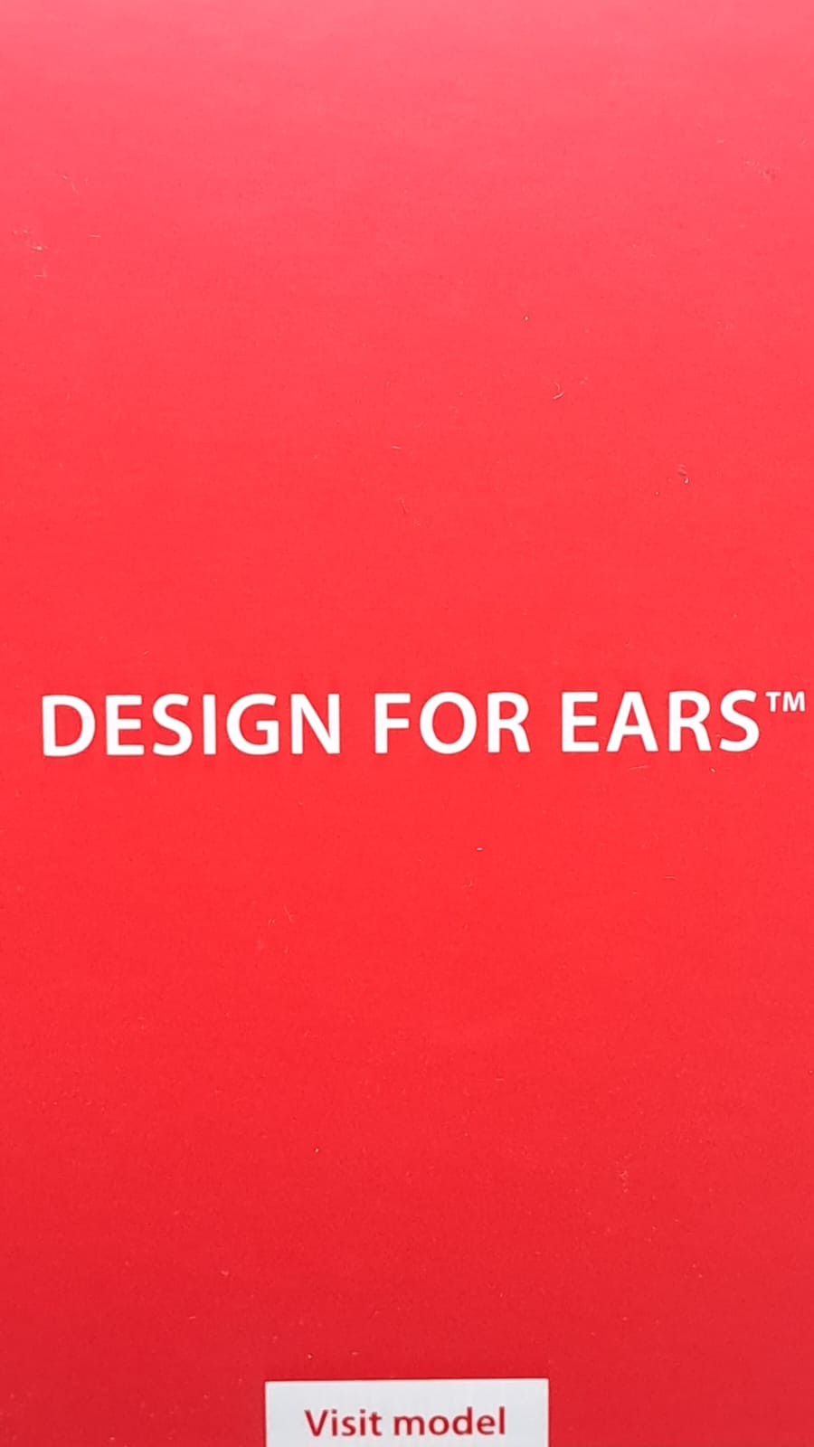 Zbliżenie czerwonego boku opakowania z białym napisem „Design for ears” i naklejką „Visit model”.