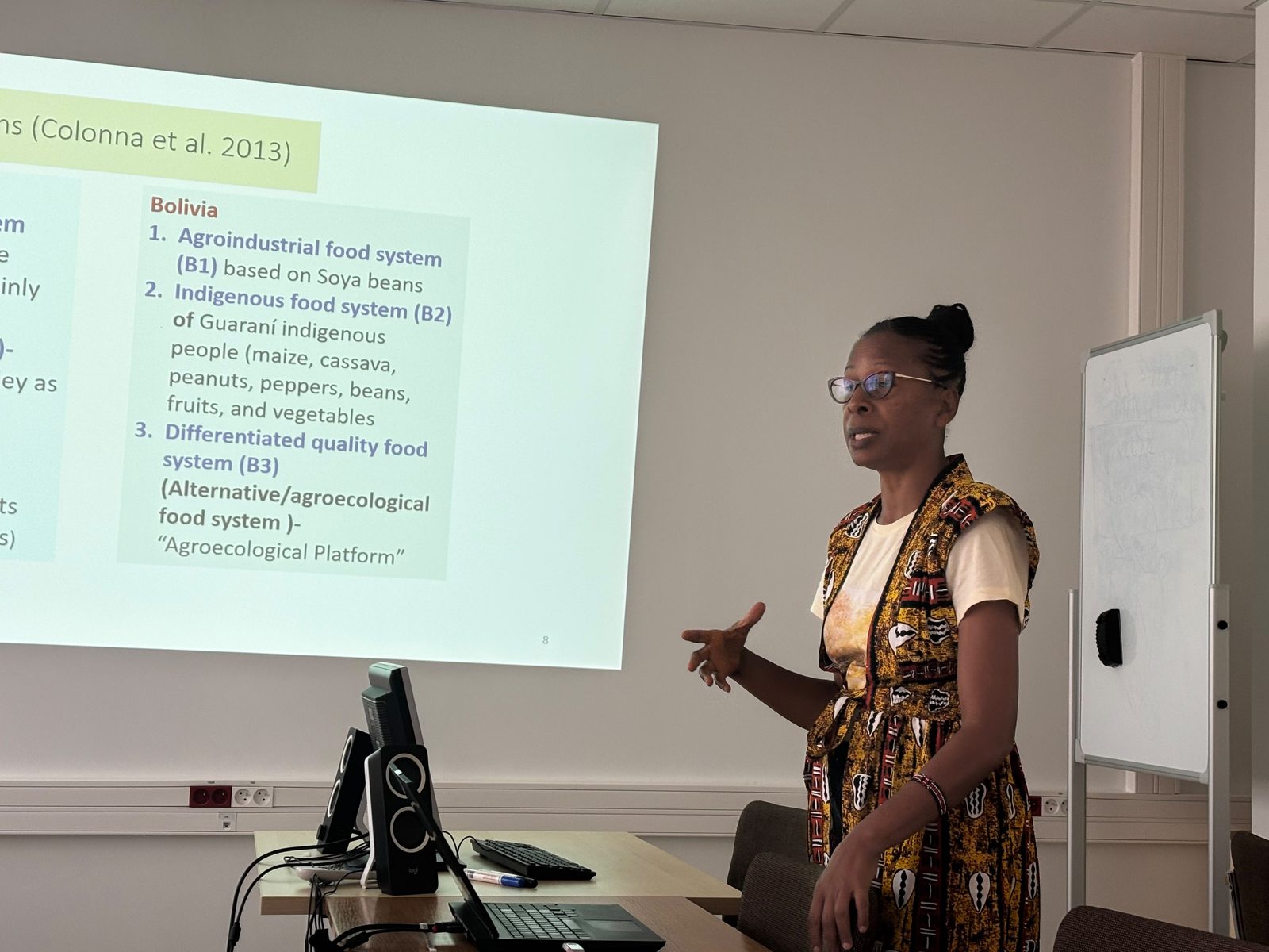 Wystąpienie podczas seminarium: osoba stojąca przy projekcji omawia slajd o systemach żywnościowych w Boliwii.